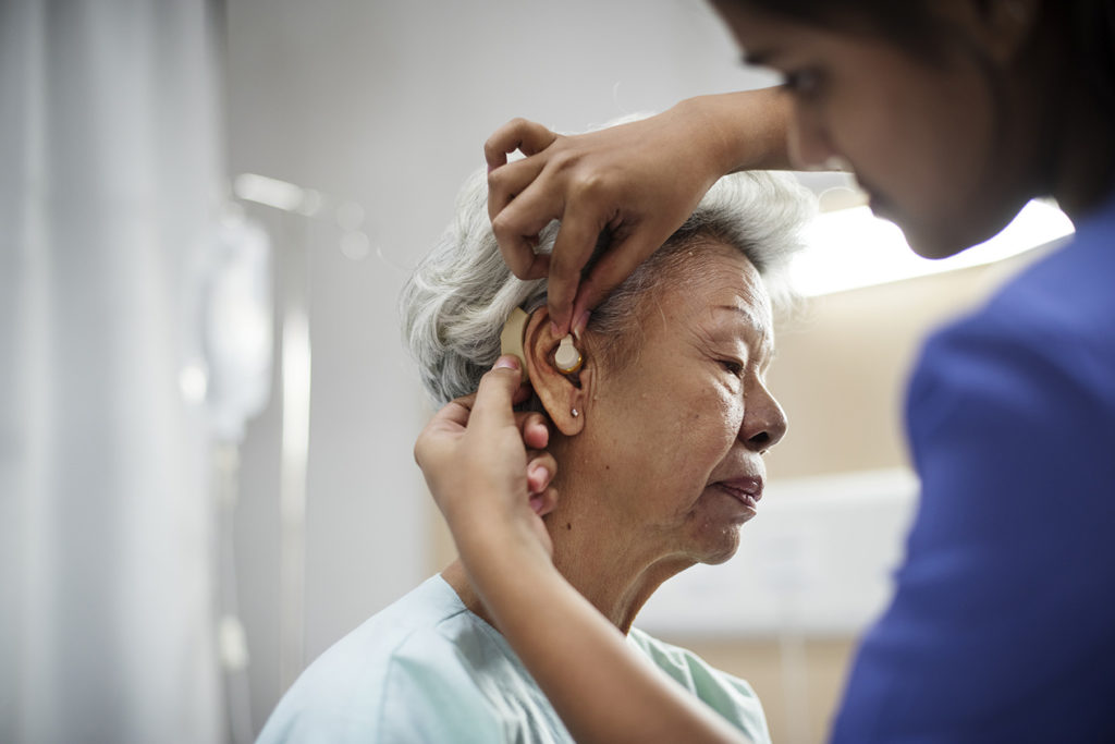 An older woman is fitted with a hearing aid.